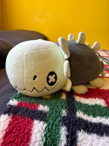 Customer's Glowing Green Lizard Plush from Rain World resting on a colorful, textured blanket.