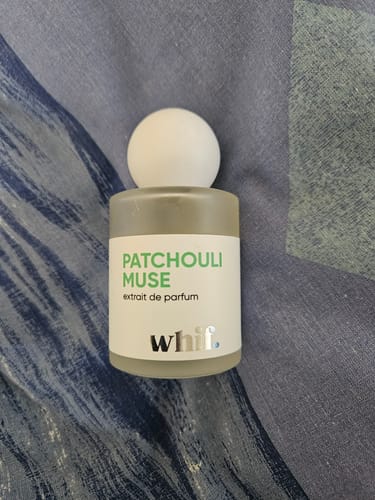 Customer's bottle of Patchouli Muse perfume by Whif., shown on a patterned fabric.