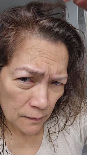 Close-up of a reviewer lifting their hair to show gray roots before using the Instant Dye Shampoo.