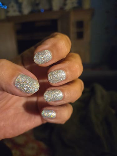 Nahaufnahme der Hand einer Kundin mit aufgetragenen, glitzernden Magician Dust Nagelfolien.
