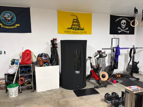Reviewer's black Sauna Pod set up in a home gym with other workout equipment.