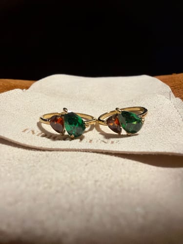 Customer's two matching Leesha Birthstone Rings with green and reddish-brown stones resting side-by-side on a pouch.