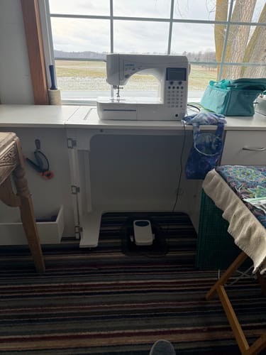 Customer's white Harriet Sewing Cabinet with a sewing machine in the flat-bed position, set up in front of a window.