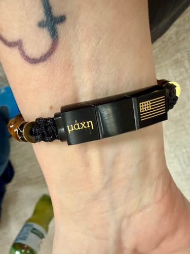 Customer wearing the Tiger's Eye Battle Beaded Bracelet, showing the black clasp with an American flag and 'μάχη' engraving.