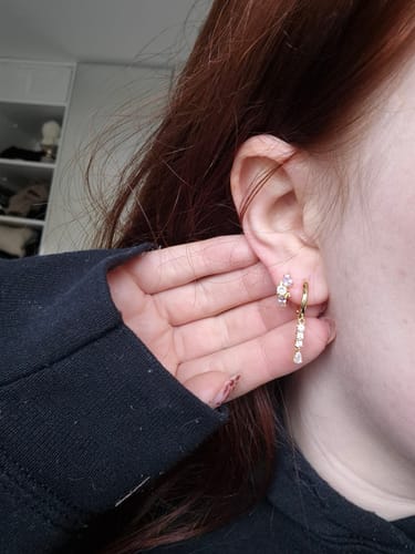Close-up of a customer's ear, showing the Cascade huggies Gold earring with its layered dangling stones.