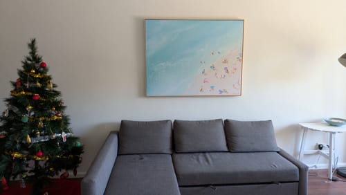Customer's Summer in Manly art print hanging on a wall above a grey sofa in a living room.