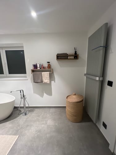 Recensent toont het houten Lila wandhanddoekrek in een badkamer, met handdoeken en producten erop.