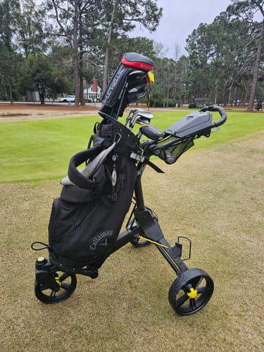 Customer's black Cybercart Push+ loaded with a golf bag and parked on a grassy golf course.