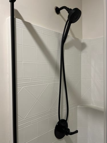 Customer's black replacement shower hose installed in a white tiled shower.