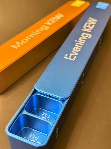 Customer's blue 'Evening' Weekly AM-PM Pill Case open, showing compartments, next to the orange 'Morning' case.