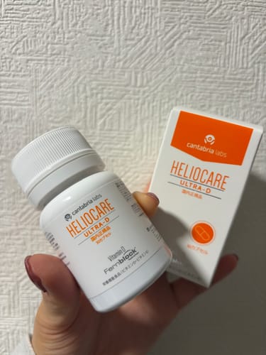 レビューアーがヘリオケア ウルトラDのボトルと箱を手に持っている様子。