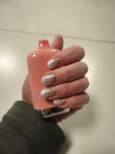 Die Hand einer Kundin mit den glitzernden UV-Gel-Folien „Babyboomer Nude Sparkle“ und einem goldenen Überlack.