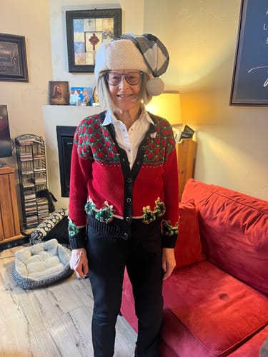 A reviewer in a festive sweater and hat standing in their living room.