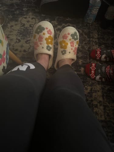 Customer's point-of-view wearing the Livia Flower Slippers with a colorful floral pattern on a rug.