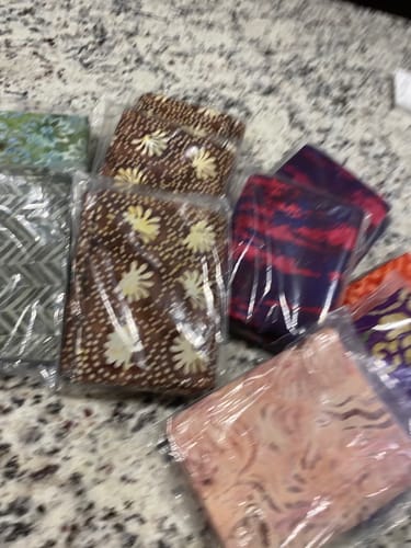 Reviewer's blurry photo of the assorted batik-style Mystery 1 Yard Fabric Cuts they received, still in clear packaging.