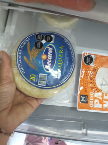 Cliente sosteniendo el paquete de tortillas de harina del Kit Carne Asada sobre un cajón de refrigerador.