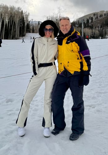 Customer wearing the white slim-fit one-piece ski suit with a black faux fur hood on a snowy slope.
