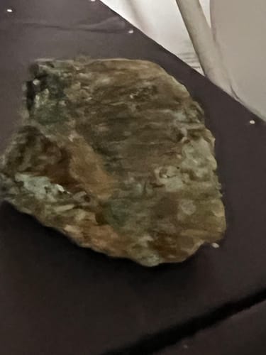 Customer's raw crystal from the VIP Crystal Club, showing green and gold tones on a dark surface.