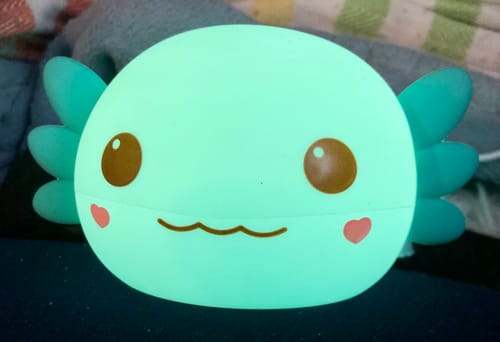 Customer's blue Axolotl squishy night light glowing with a soft green light in a dark room.