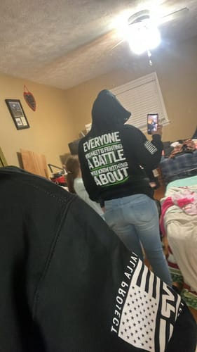 Customer wearing the black Be Kind - Hoodie from the back, showing the inspirational quote in white and green letters.