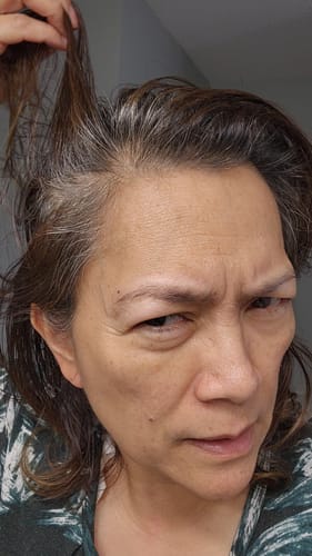 Reviewer lifts their hair to show about an inch of stubborn gray root growth before treatment.