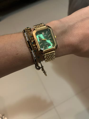 Customer wearing the CLAIRE DE MAINS watch, showing its rectangular green face and gold-colored band on their wrist.