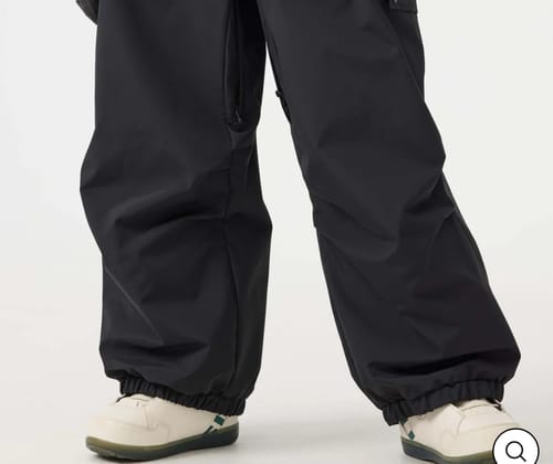 Reviewer showing a close-up of the baggy black snow pants, focusing on the elastic ankle cuffs and overall fit.