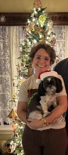 Reviewer wearing the maple Judy Blue wide leg jeans while holding a small dog by a Christmas tree.