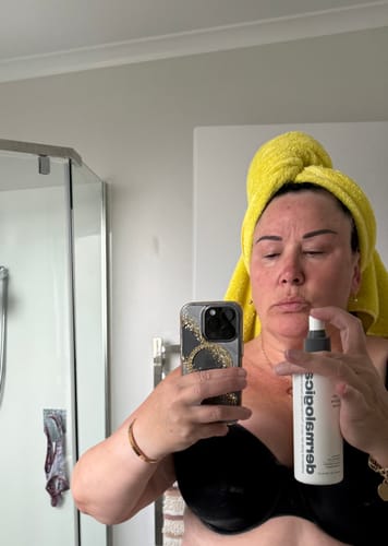 Reviewer with a towel-wrapped hair, taking a mirror selfie while holding the multi-active toner, ready to spray.