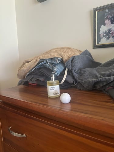 Reviewer's bottle of Azure Spice fragrance with the cap off, sitting on a wooden dresser next to a pile of clothes.