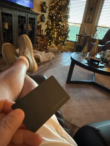 Customer holding the black SPOTMINDERS Tracking Card while relaxing in a living room with a Christmas tree.