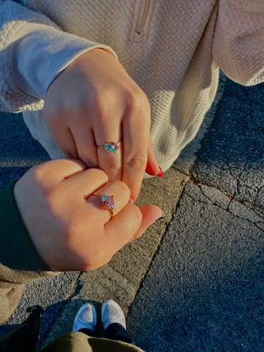 Customer shows two dainty, sparkly Leesha Birthstone Rings on two hands held together outdoors.