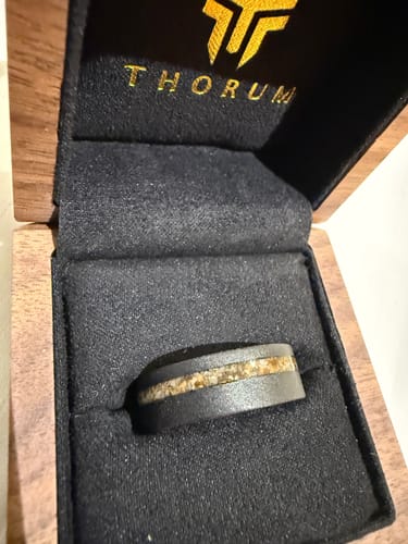 Customer's Thorum ring in its open, branded wooden box. The dark ring features a textured, light-colored inlay.
