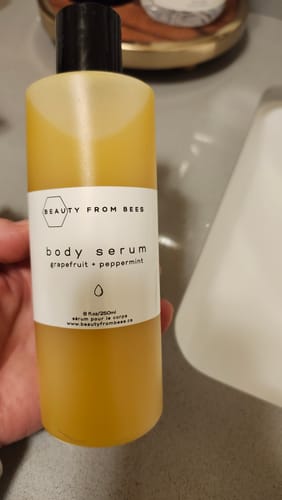 Customer holding the Body Serum bottle. The label reads 'grapefruit + peppermint' and the yellow liquid is visible inside.