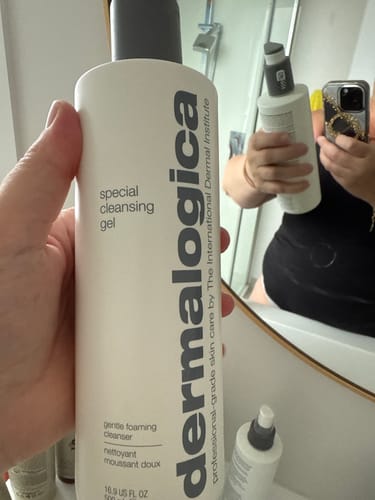 Reviewer holding a large white bottle of special cleansing gel in a bathroom.