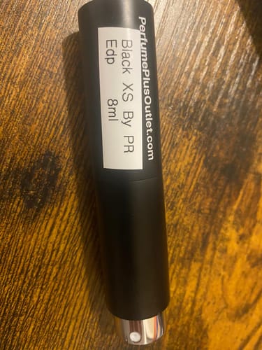 Customer's black travel spray bottle of Black XS for Men perfume on a wooden surface.