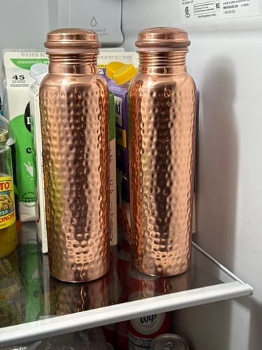 Reviewer's two hand-hammered Pure Copper Water Bottles sitting on a shelf inside a refrigerator.