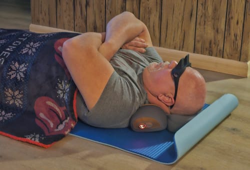 Customer lying on a floor mat using the powered-on Thera Pillow traction massager for neck relief.