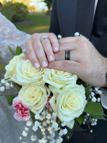 Reviewer's hands showing the black The Legend ring with a rose gold inlay over a bouquet of white roses.