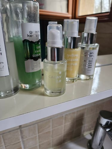 Photo d'une cliente montrant son huile pour le visage Cacay 2.0 sur une étagère de salle de bain parmi d'autres produits.