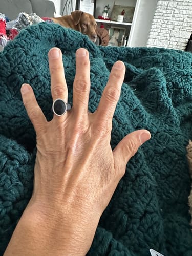 Customer's hand wearing the black Oversize Oval Silicone Ring against a dark green blanket.