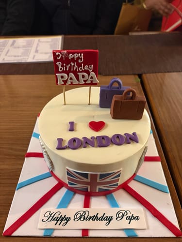 Customer's England UK Theme Cake on a table, with 'I Love London' text, a UK flag, and two fondant suitcases on top.