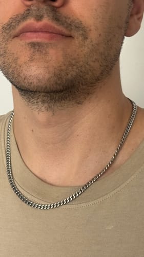 Primer plano de un cliente que lleva la Cadena Miami Cuban de 5 mm sobre una camiseta beige.