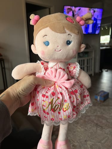 Customer holding a soft Personalized Strawberry Girl doll with 'Nova' embroidered in gold on its pink, strawberry-print dress.