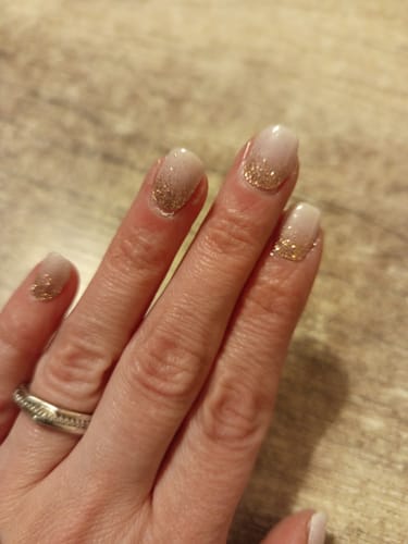 Hand einer Kundin, die ihre Maniküre mit dem UV Gel 'Babyboomer Nude Sparkle' mit glitzerndem Nude-Design zeigt.
