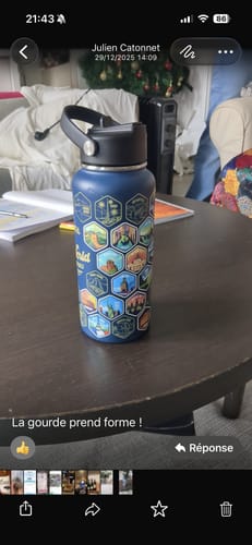 Customer's blue World Explorer Bottle with many colorful travel stickers applied, standing on a dark table.