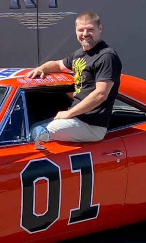 Customer wearing the black Italian Stallion Logo Rocky T-Shirt while sitting on the door of an orange car.