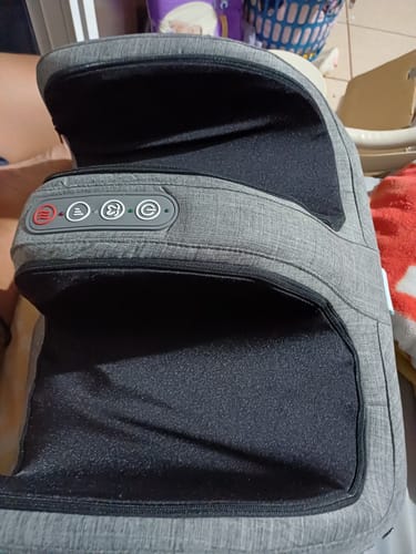 Un cliente muestra el masajeador para pies y pantorrillas Homedics. El aparato es de tela gris con interior negro y panel de control.