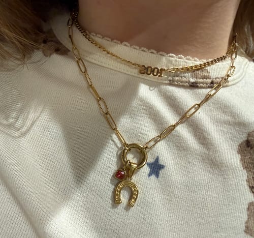 Reviewer wearing the gold Lucky Birthstone Necklace with horseshoe and red birthstone charms, layered with a second chain.