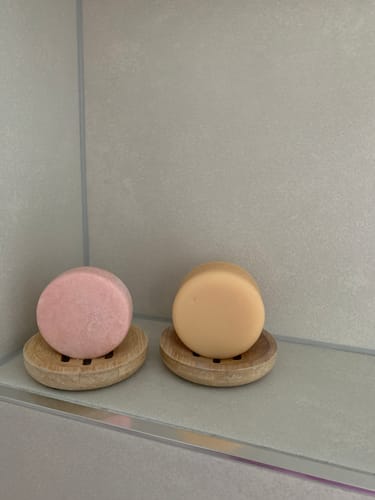 Customer's yellow Ginger Conditioner Bar and a pink shampoo bar on two wooden dishes in a tiled shower.